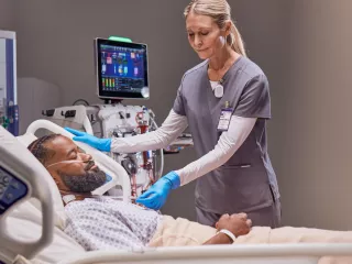 Healthcare provider at the patient's bedside, with a PrisMax device in the background.