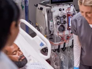 Two healthcare professionals at the patient bedside in front of the PrisMax system